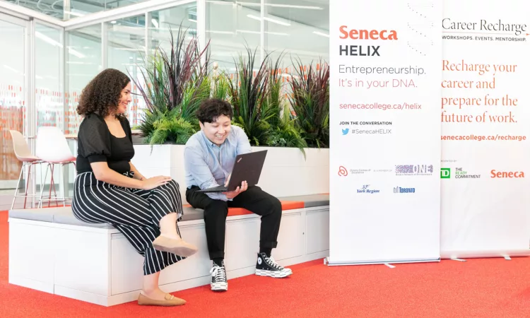 Seneca HELIX - One person showing something on a laptop to another while sitting on a bench